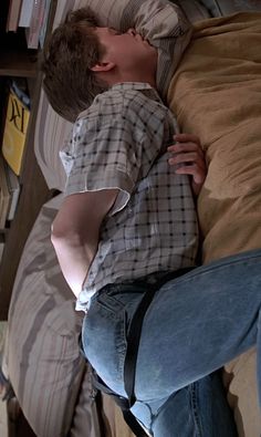 a young man sleeping on top of a bed next to a book shelf filled with books