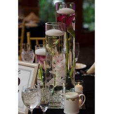 flowers and candles are arranged in tall glass vases on a table with other items