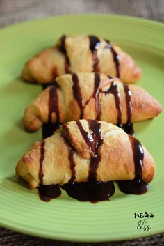 three croissants with chocolate drizzled on them sitting on a green plate