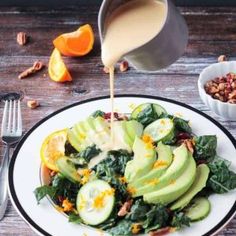 someone pouring dressing onto a salad with avocado, oranges and pecans