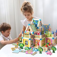 two children playing with a large building set on a table in front of a white curtain