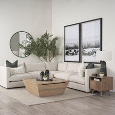 a living room with white couches and wooden coffee table in front of two framed pictures