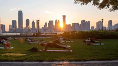 many people are doing yoga in the park near the water and cityscape at sunset