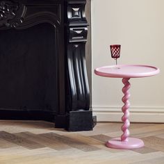 a pink table sitting in front of a fireplace with a candle on top of it