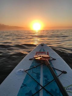 the sun is setting over the ocean from a surfboard in the water, with an oar resting on it's side