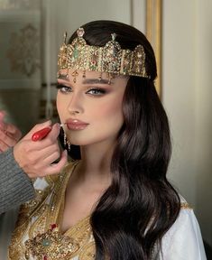 a woman getting her make up done by a man in an ornate dress and tiara