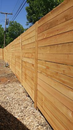 a wooden fence that is next to some gravel and trees in the background with power lines above it