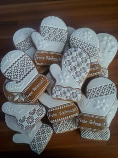 several decorated cookies in the shape of mittens on a wooden table with brown and white trimmings