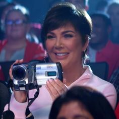 a woman holding up a video camera in front of her face and people behind her