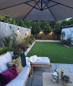 an outdoor patio with white couches and green grass in the back yard, next to a wooden table