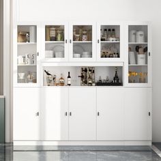 a white cabinet with lots of bottles and glasses on it in a room that has marble floors