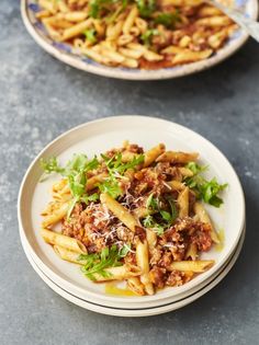 two plates filled with pasta and meat on top of a table