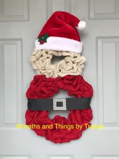 a christmas wreath with a santa hat hanging on the front door and attached to it