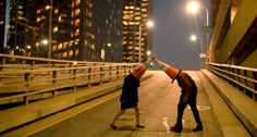 two people standing in the middle of a street with their hands up to each other