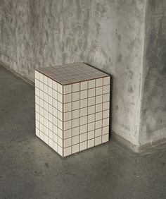 a white and brown cube sitting on the ground next to a cement wall in an empty room