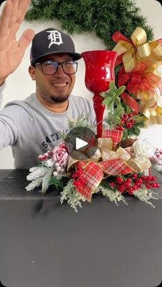 a man wearing a hat and glasses standing in front of a christmas wreath with his hands up