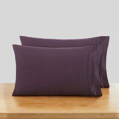 two pillow cases sitting on top of a wooden table next to each other with purple sheets