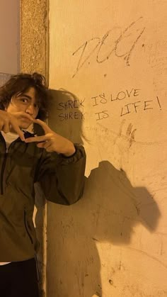 a young man leaning against a wall with his finger in his mouth and writing on the wall behind him