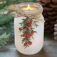 a mason jar with holly and berries on the lid is sitting next to pine cones