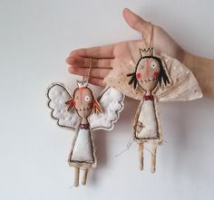 two handmade angel ornaments hanging from the palm of someone's hand