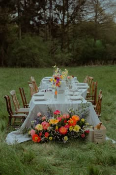 an outdoor table set up with flowers and candles for a dinner party in the grass