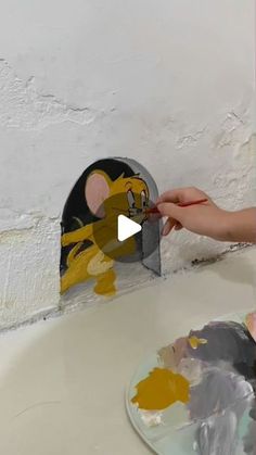 a person is painting a cartoon mouse on a piece of paper with acrylic paint