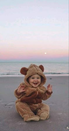 a baby in a bear costume sitting on the beach