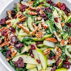 a salad with apples, cranberries and pecans in a white bowl on a table