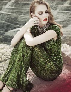 a woman sitting on top of a rock next to a body of water with her hands under her face