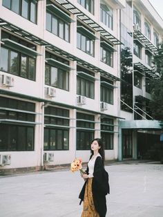 a woman standing in front of a building holding a donut and looking up at the sky