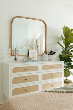 a white dresser topped with lots of drawers next to a mirror and potted plant