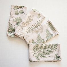 four napkins with green leaves on them sitting on a white tableclothed surface