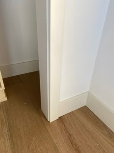 the corner of a room with a wooden floor next to a white wall and an open door