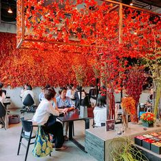 people sitting at tables with red flowers hanging from the ceiling