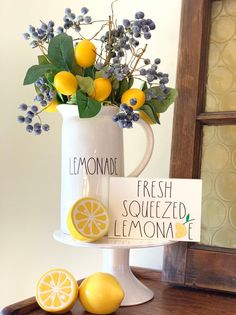 a white vase filled with lemons and flowers on top of a wooden table next to a sign that says lemonade