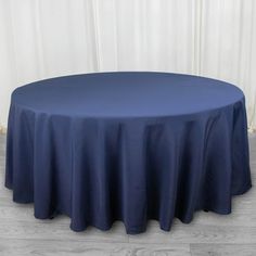 a round table with a blue cloth on it in front of a white wall and wooden floor