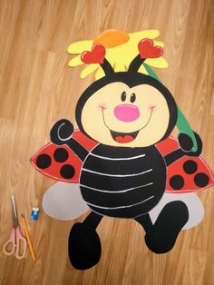 a ladybug cut out sitting on top of a wooden floor next to scissors