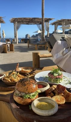 a wooden table topped with plates of food next to a beach covered in umbrellas