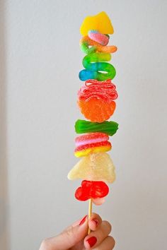 a person is holding up a rainbow lollipop with gummy bears on it