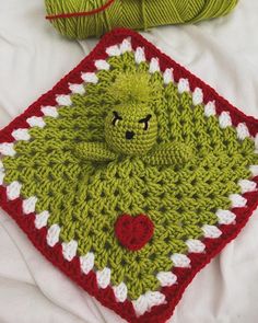 a green crocheted teddy bear sitting on top of a red and white blanket