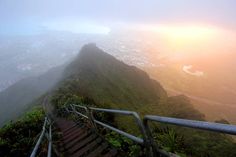 stairs leading up to the top of a mountain with fog in the air and sun shining down