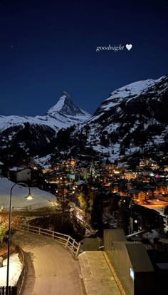 a night time view of a city with mountains in the background and snow on the ground