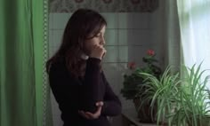 a woman standing in front of a green curtain next to a potted plant on a window sill