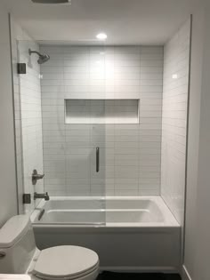 a white toilet sitting next to a bath tub in a bathroom under a light fixture