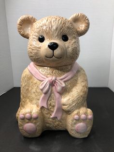 a ceramic teddy bear with a pink ribbon around its neck sitting on a black surface