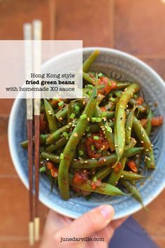 a person holding a bowl of green beans with chopsticks in front of them