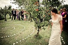 a woman in a wedding dress standing next to an apple tree surrounded by white pebbles