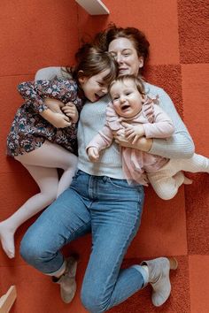 three women and one baby are laying on the floor with their arms around each other