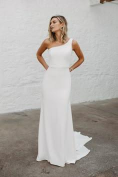 a woman wearing a white dress standing in front of a white wall and looking off to the side