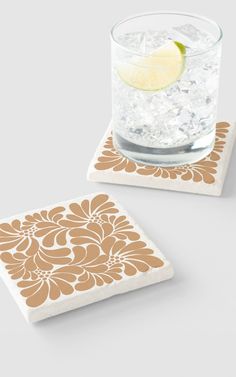 two square coasters with an orange and white floral design on the front, one has a